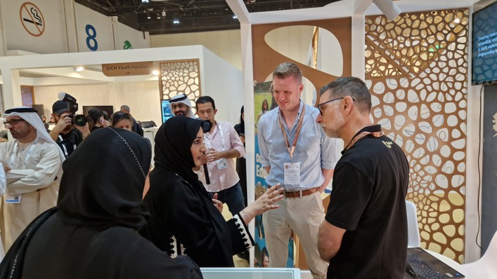 Image shows a woman in a black headscarf talking to representatives from Chester Zoo at a booth decorated with animal imagery