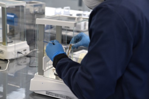 A picture of a scientist measuring out a faecal sample using lab equipment. She is wearing blue gloves.